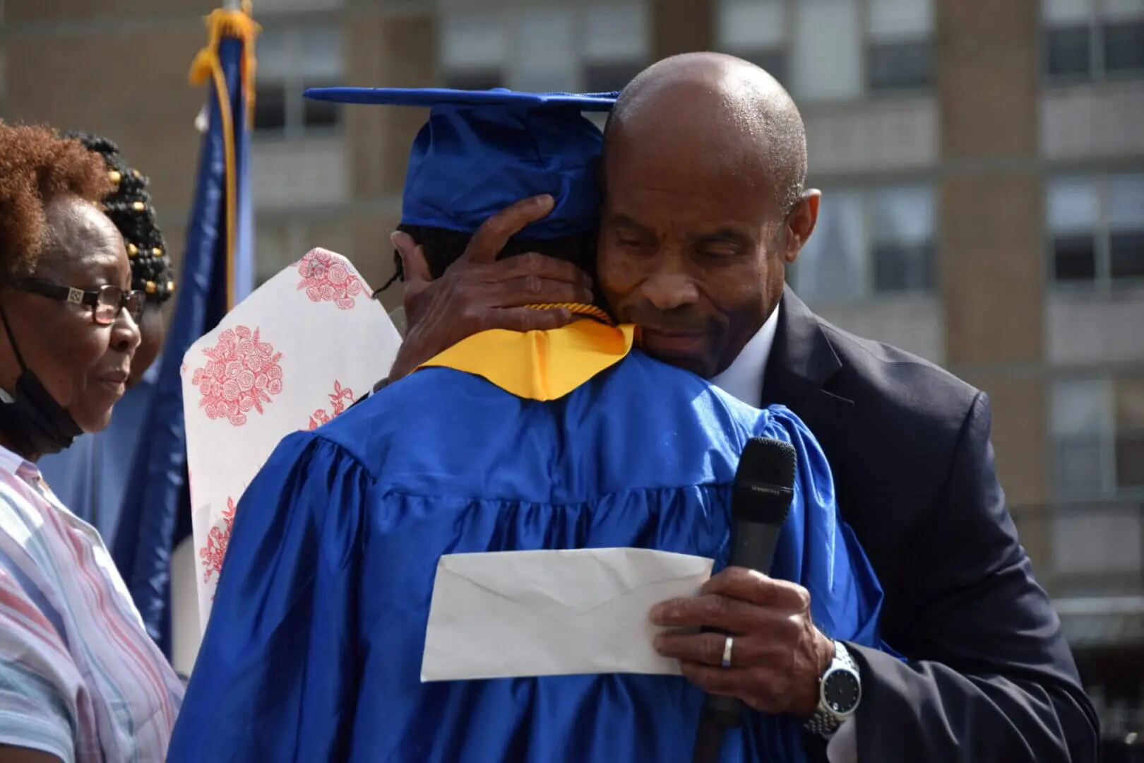 A graduate embraces a man, likely a mentor or family member, during graduation.