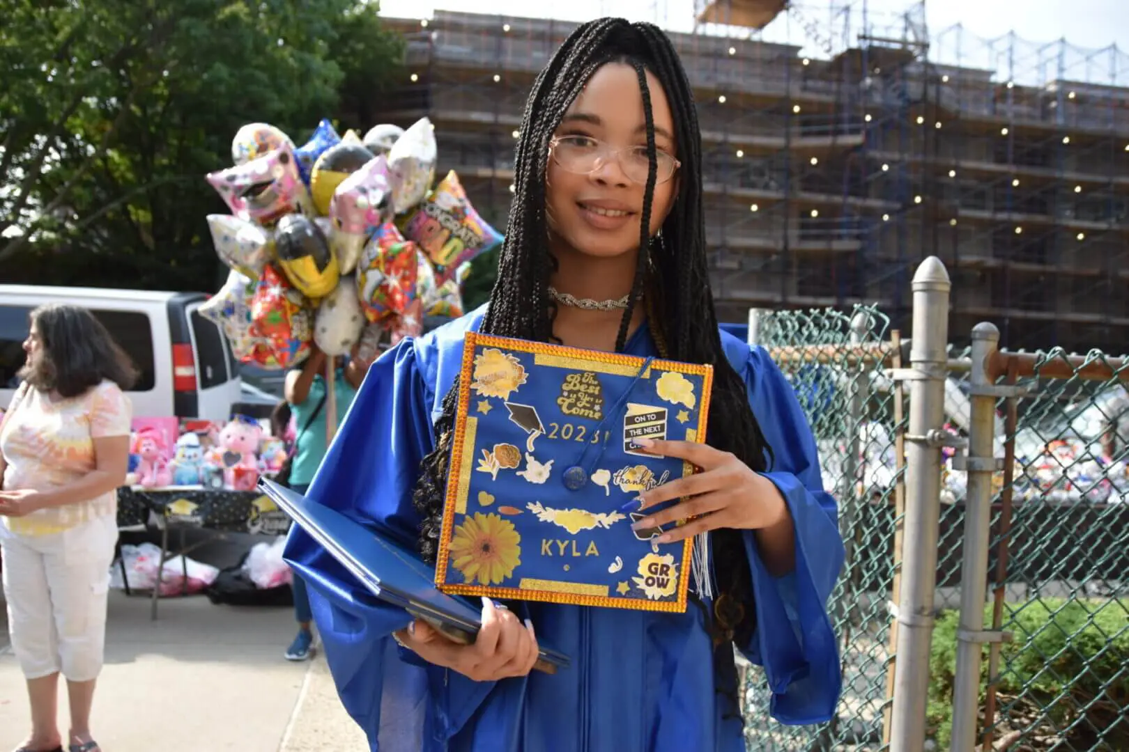 Young woman in blue graduation gown holding diploma and flowers.