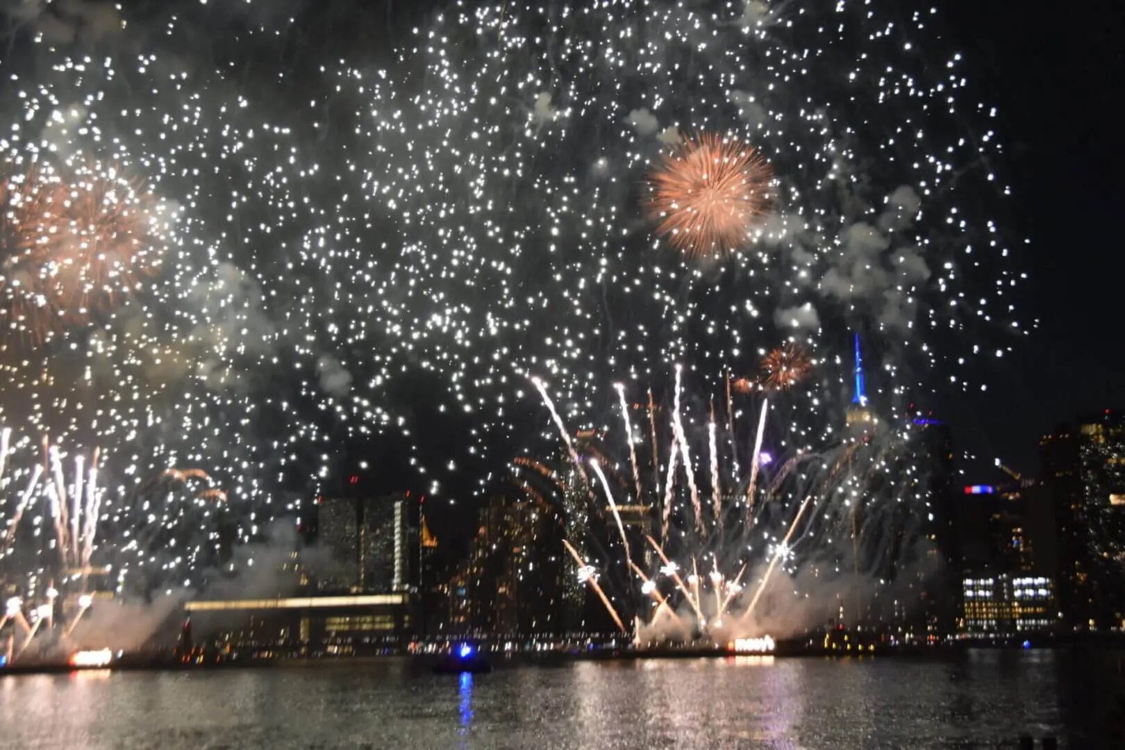 Fireworks explode brightly over water at night.
