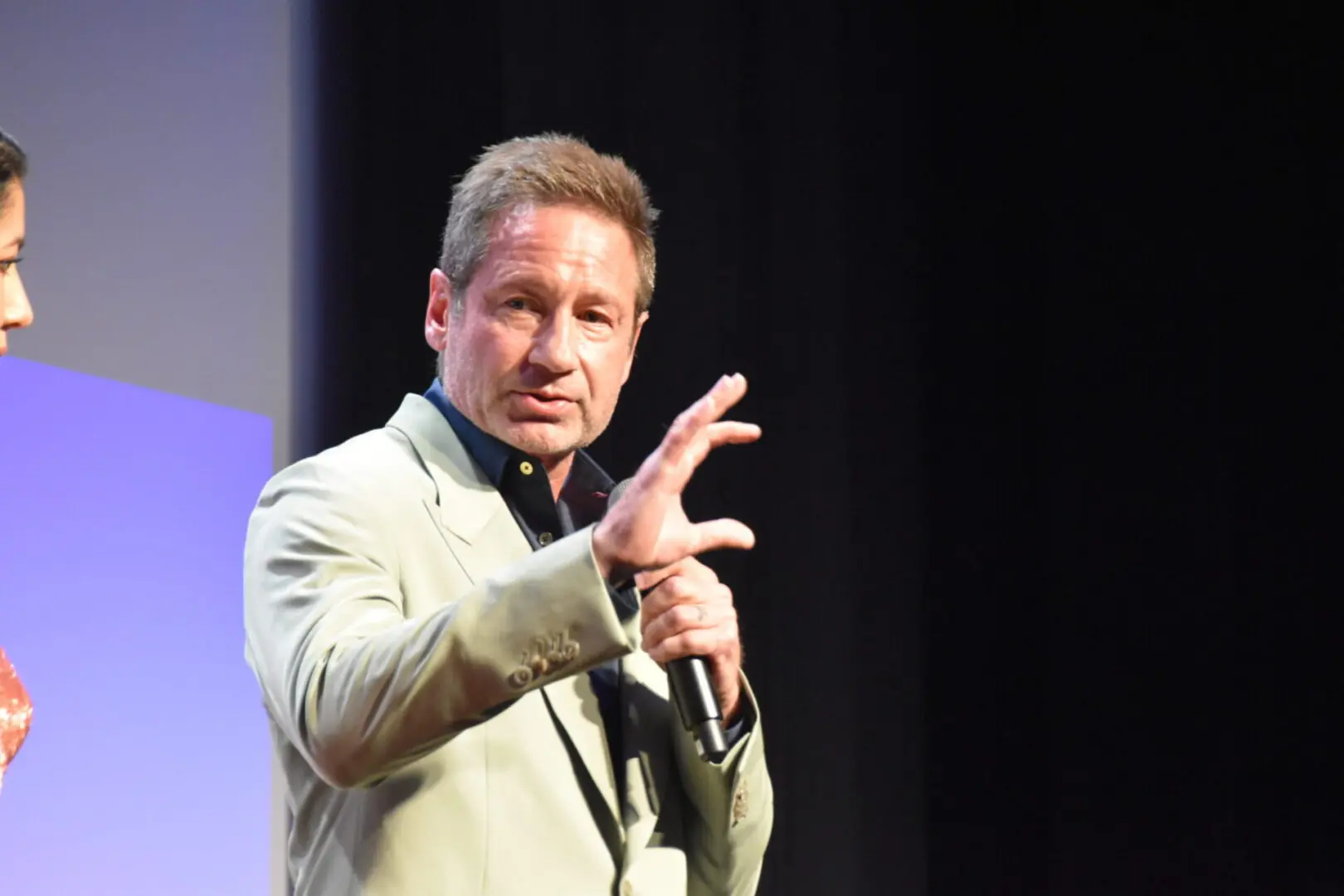 Man speaking passionately on stage with expressive hand gestures.