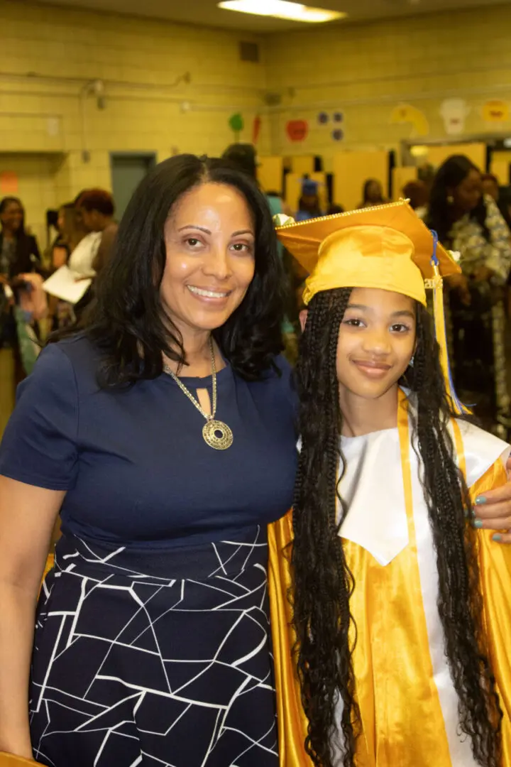 A proud woman poses with a young graduate in a yellow cap and gown.