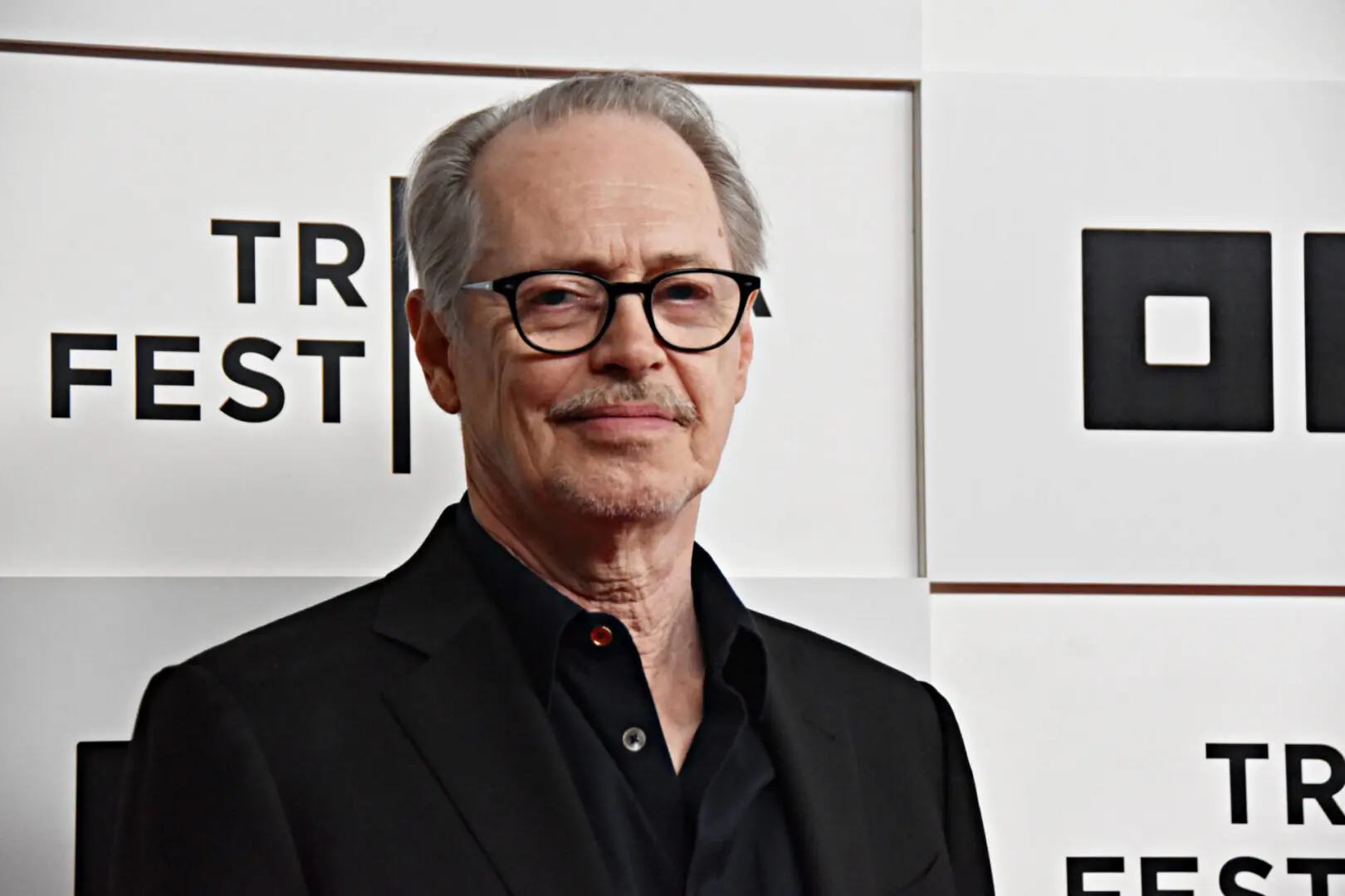 An older man with glasses in a black suit at an event.