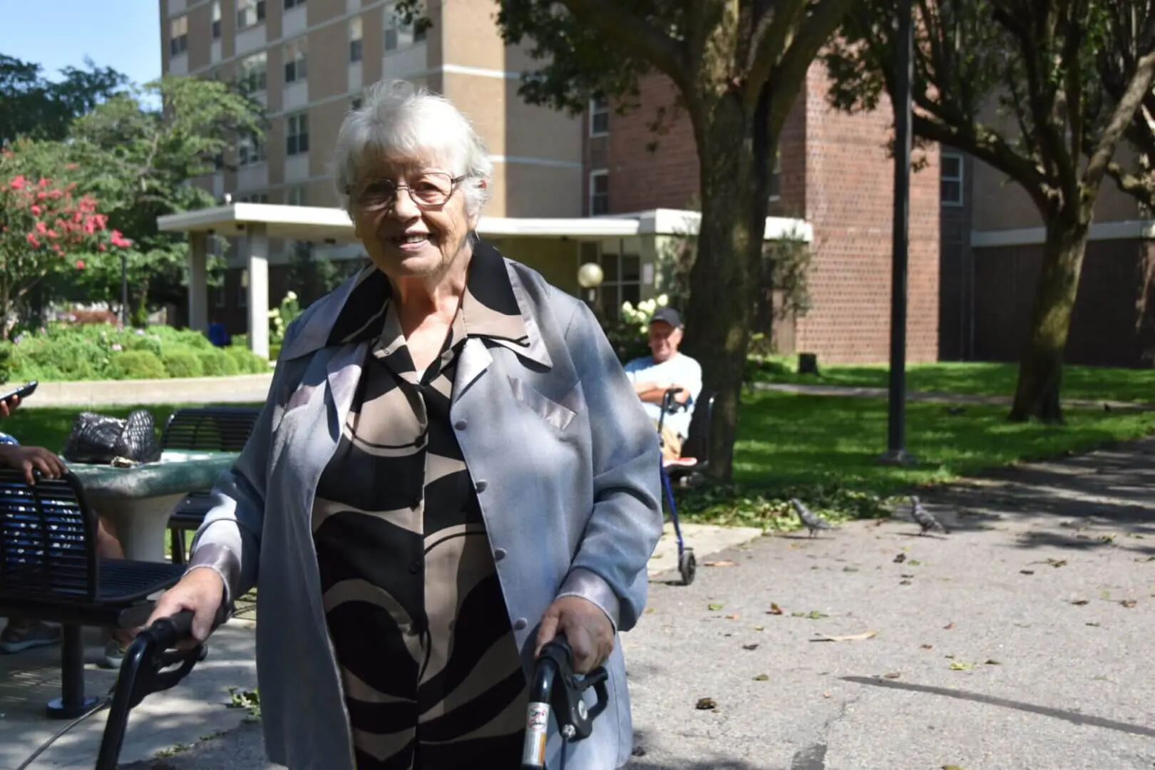 Elderly woman walking outdoors using a walker on a sunny day.