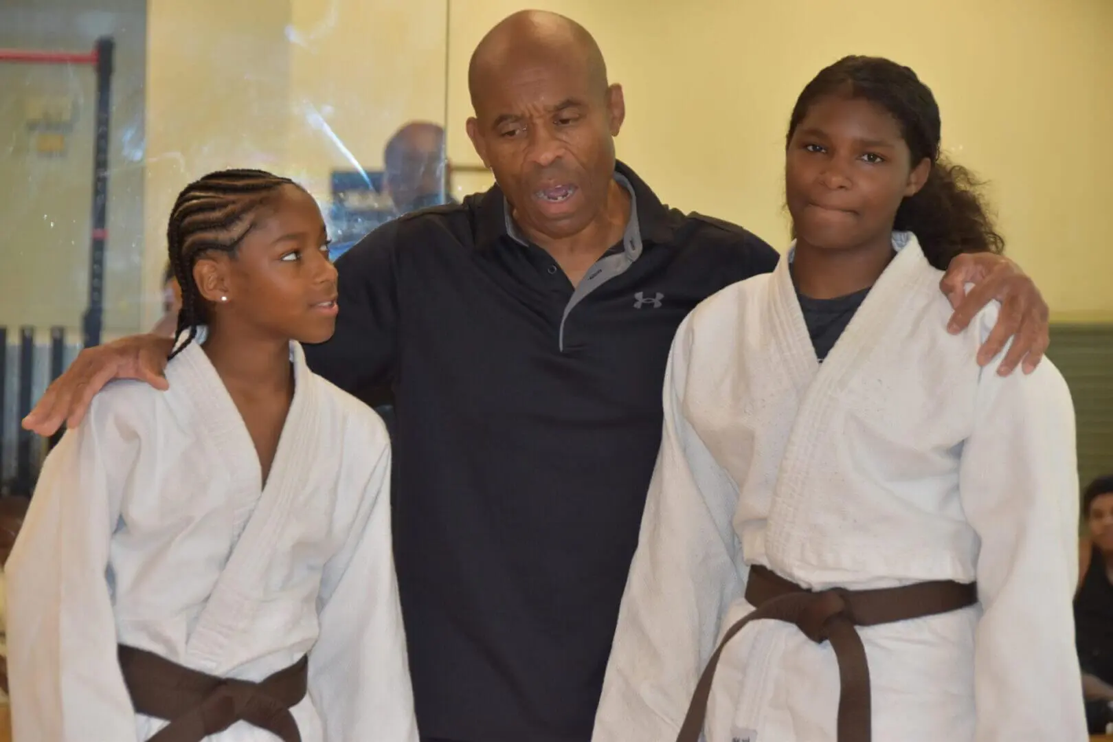 Two young martial artists in white uniforms with a coach in a blue shirt.