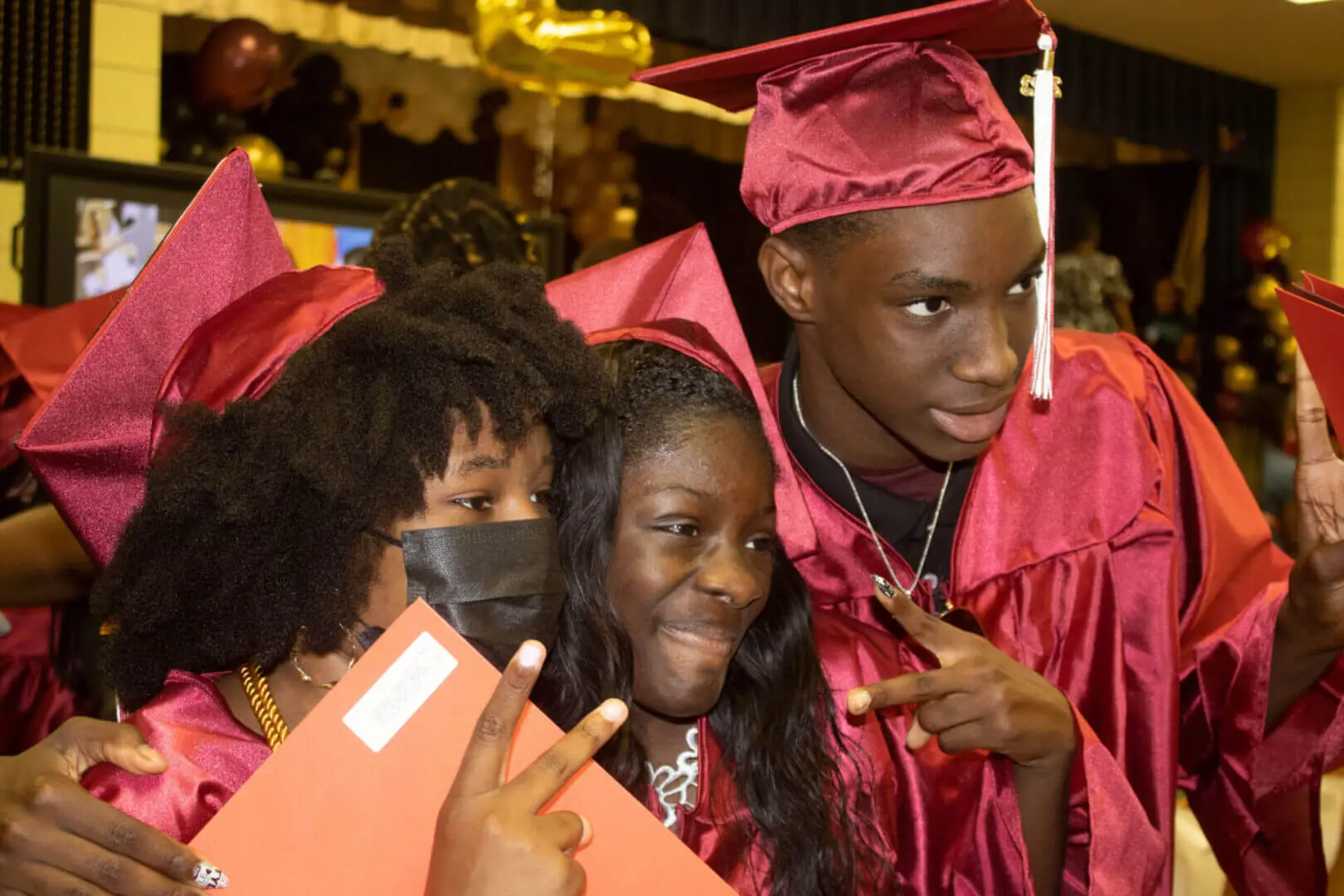 Three graduates in caps and gowns smiling and celebrating together.