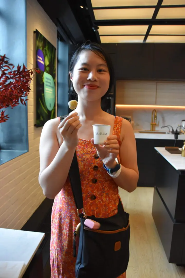 A smiling woman enjoying a drink indoors, holding a spoon and cup.