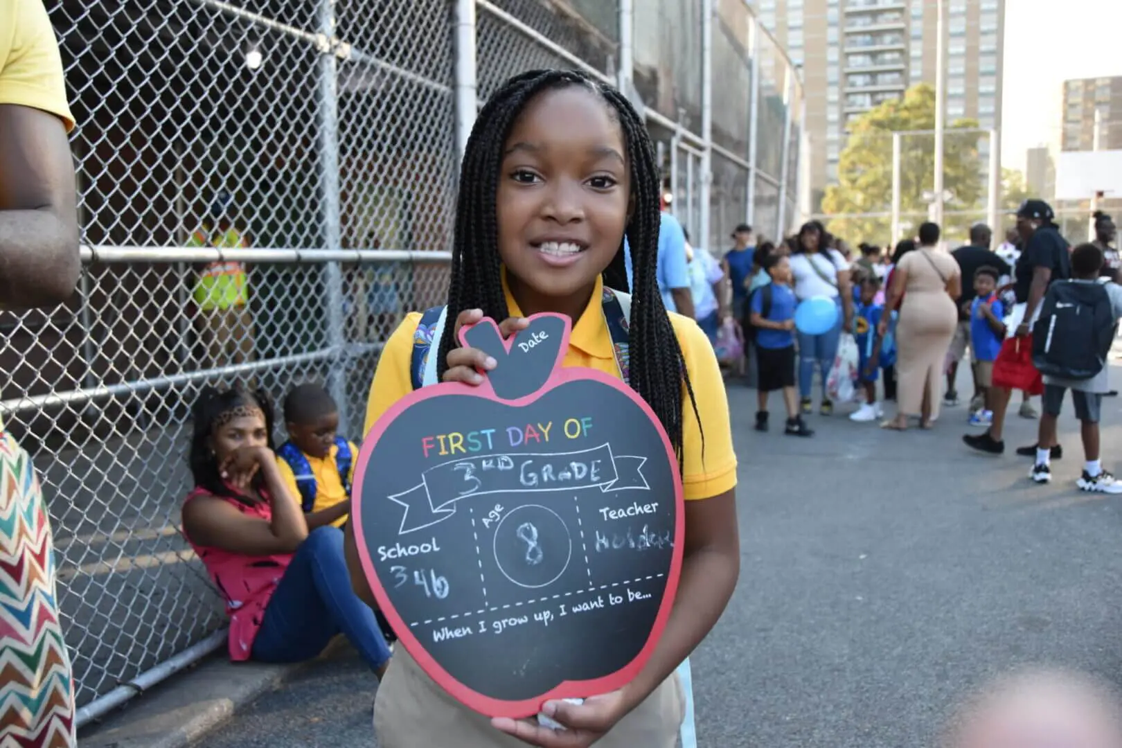 Young woman holding heart-shaped chalkboard with positive message on city street.