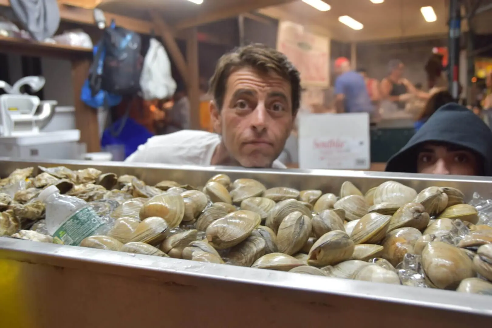Man behind a counter filled with fresh clams at a seafood market.