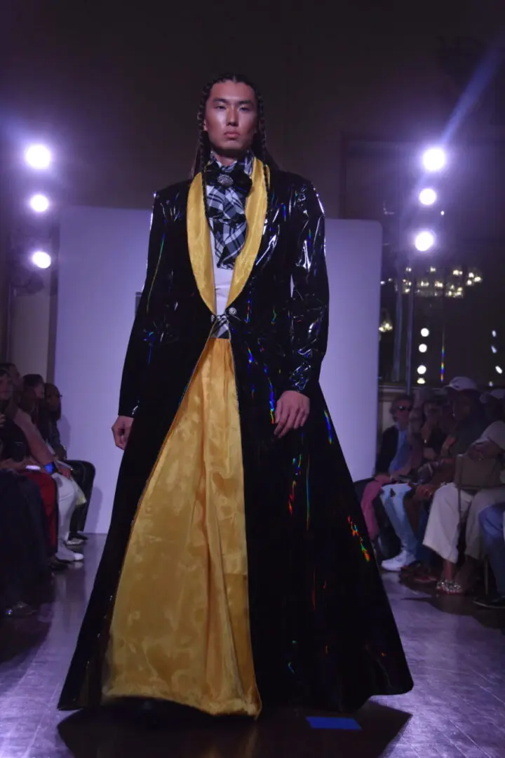 Model showcases an elegant black and yellow evening gown on the runway.