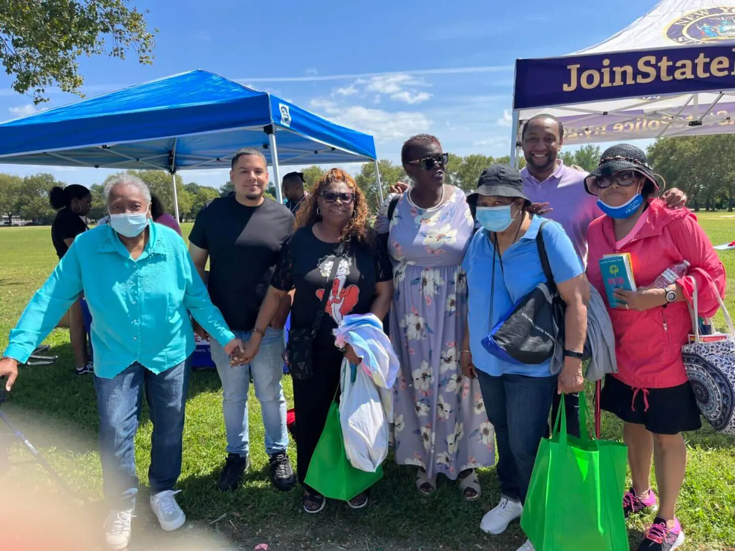 A group of people standing outdoors at an event, some holding green bags.