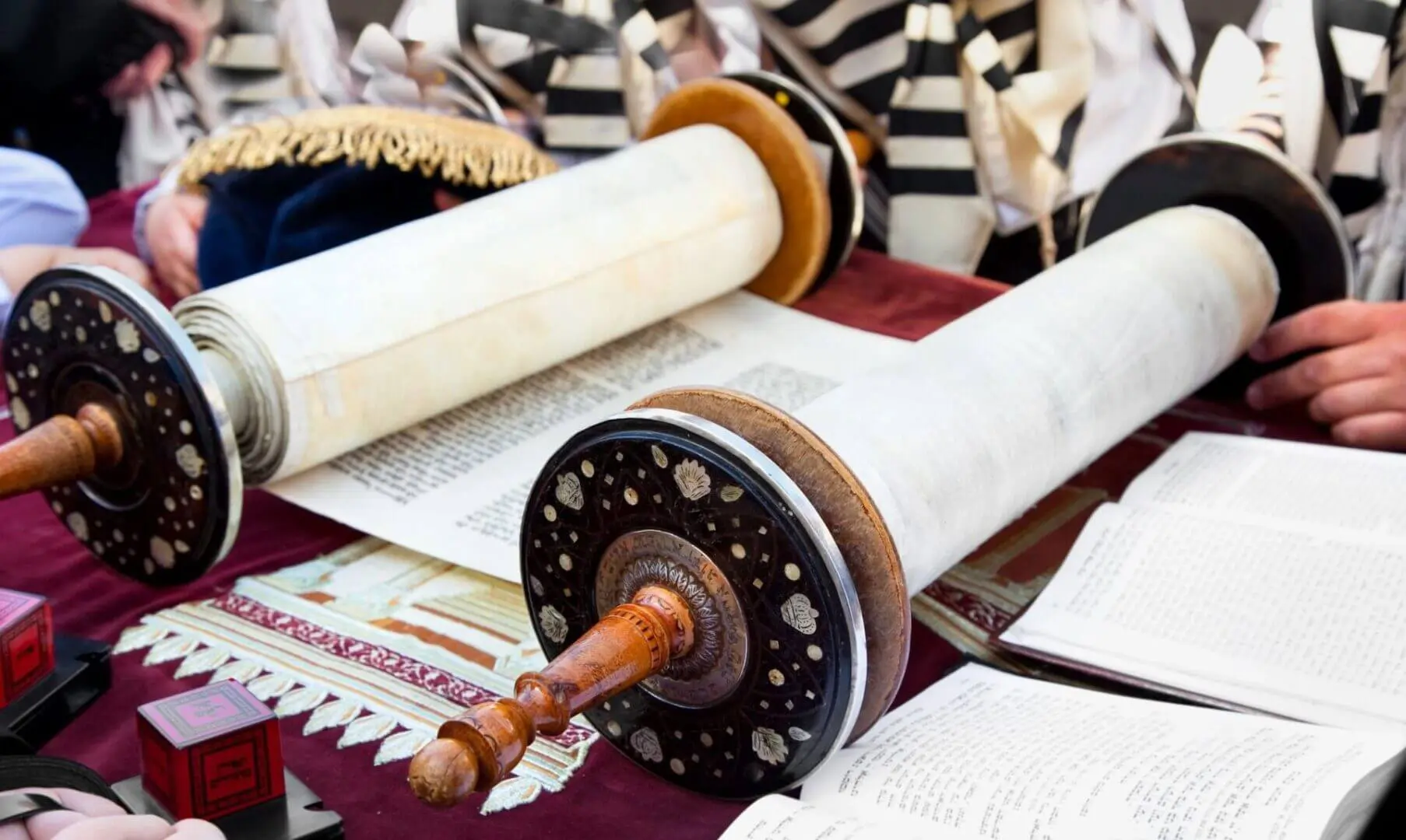 A Torah scroll partially unrolled on a table with a prayer book beside it.