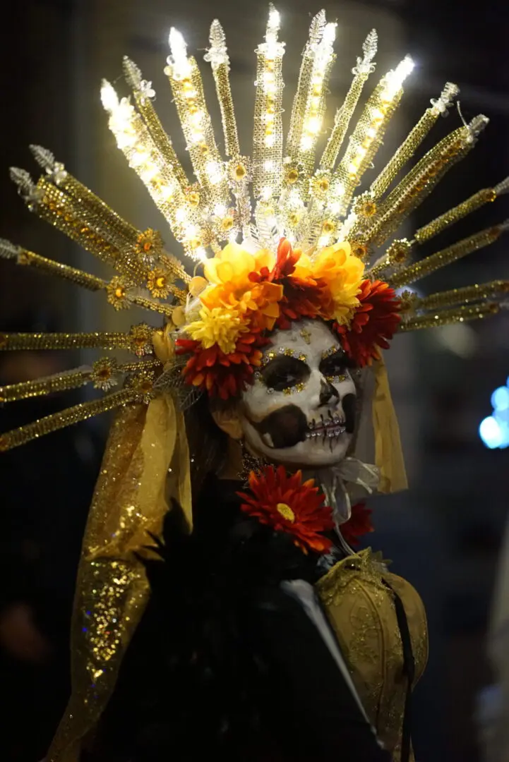 Person in elaborate Day of the Dead skull makeup and floral headdress.