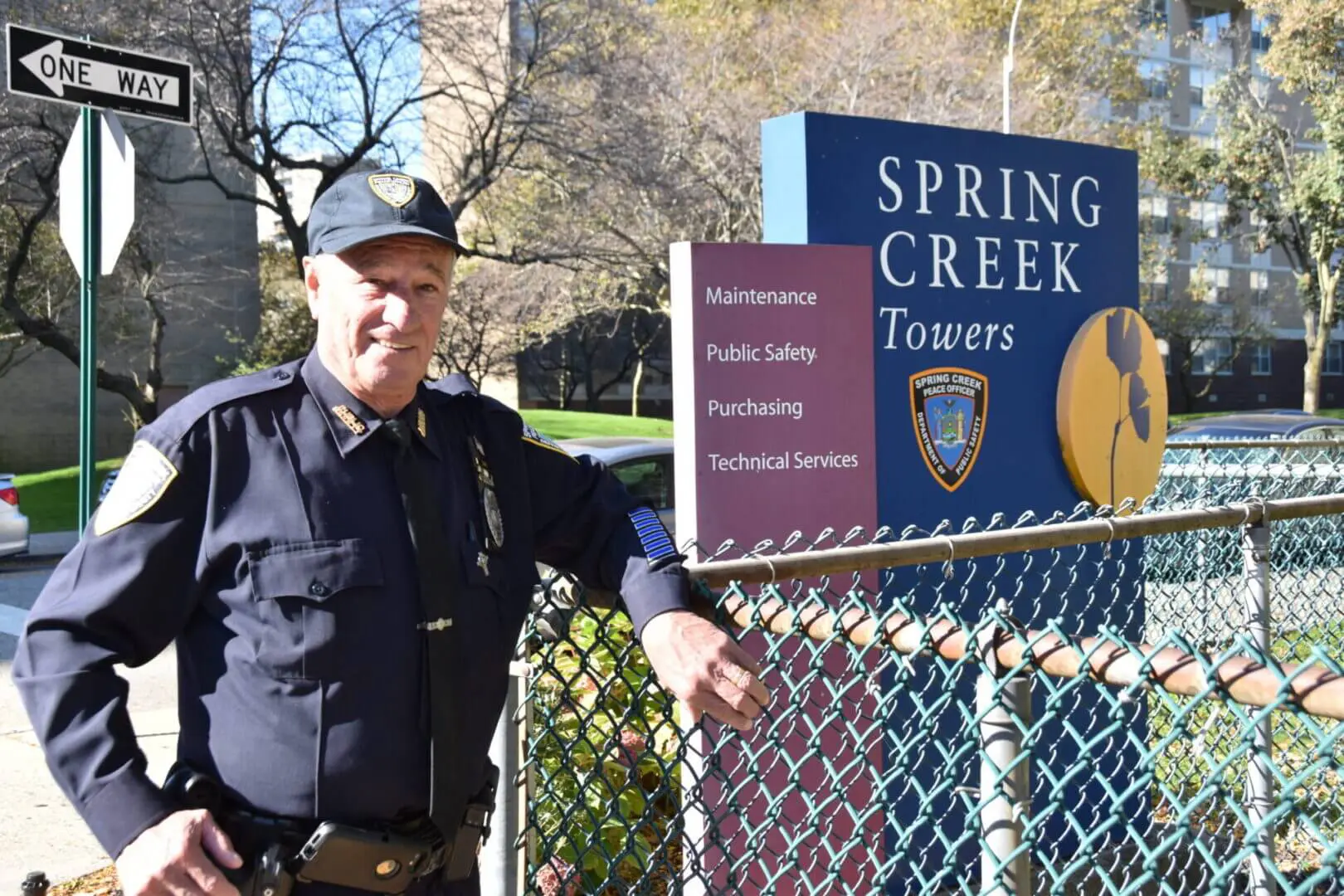 Security guard standing by the Spring Creek Towers sign and fence.