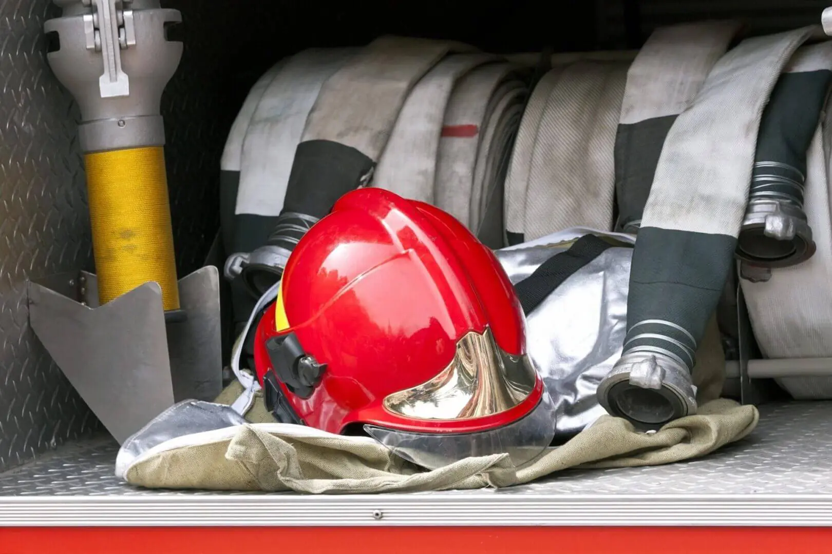 Red firefighter helmet and gear inside a fire truck compartment.
