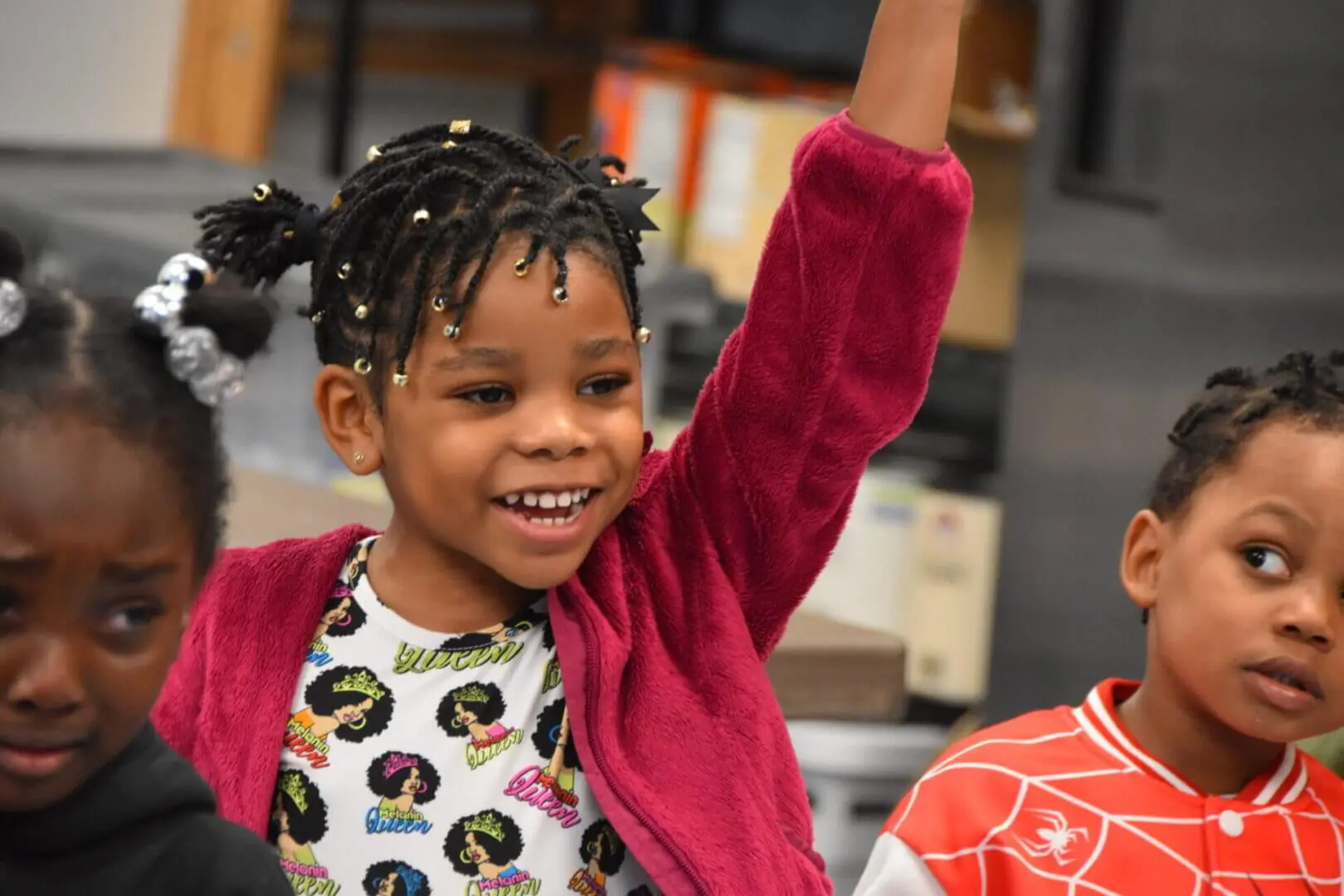 Joyful child raising hand, smiling brightly indoors.
