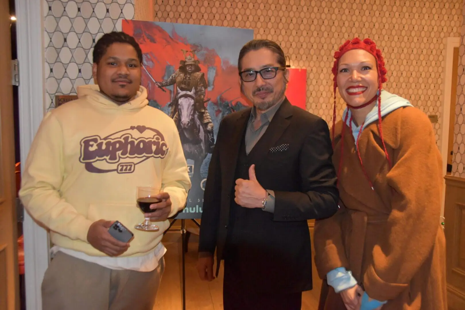 Three people posing cheerfully indoors, one holding a glass of wine.