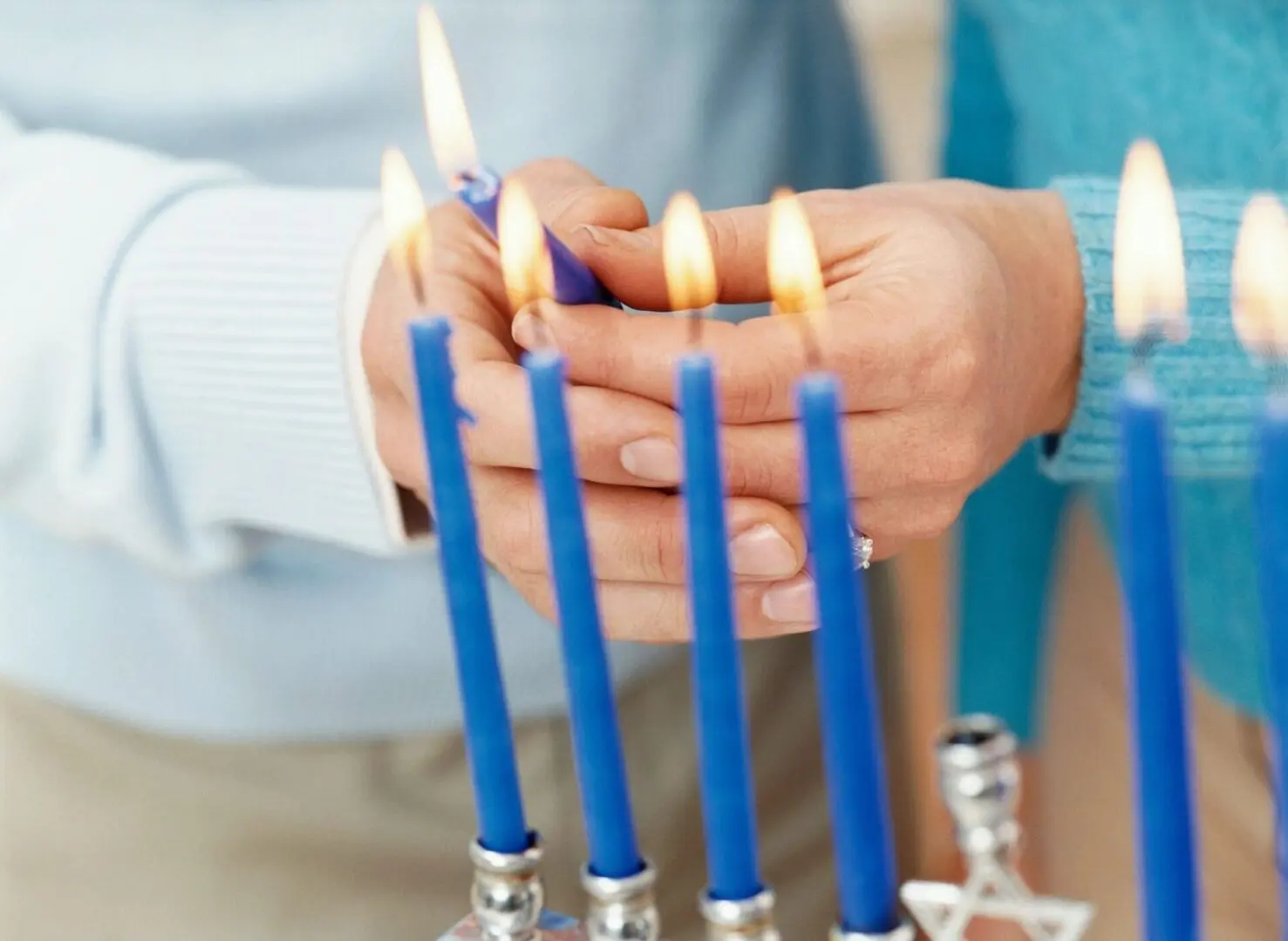 Person lighting blue Hanukkah candles on a menorah.