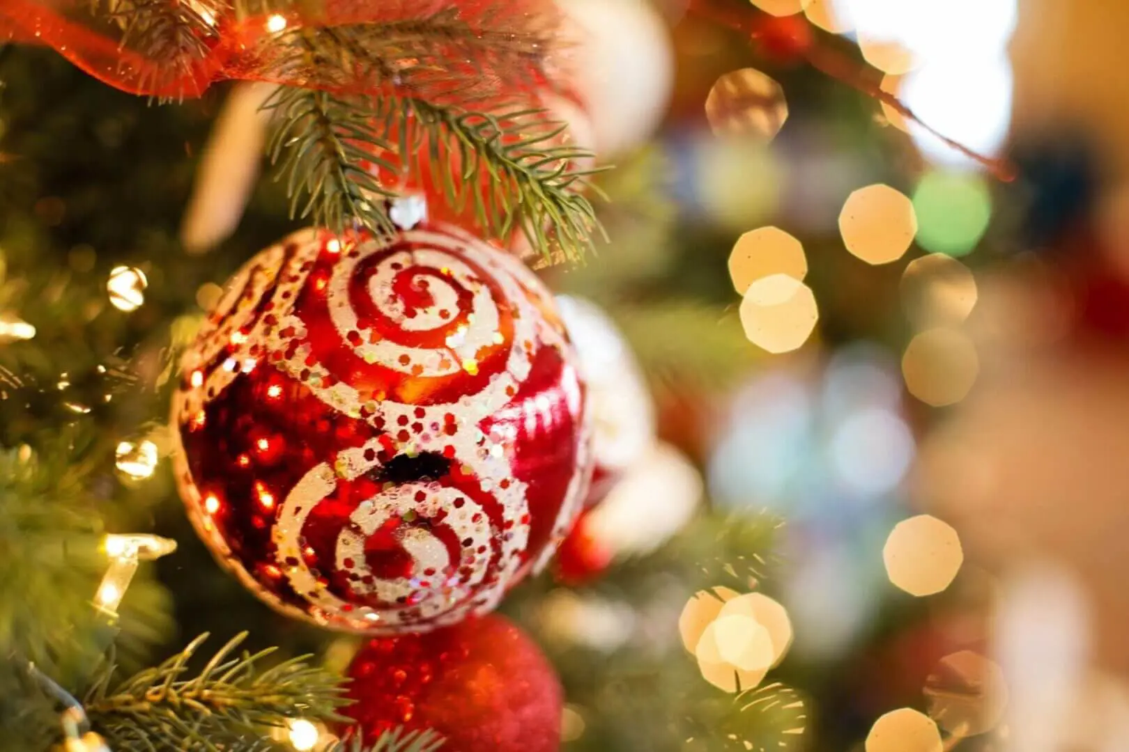 A red and white Christmas ornament hanging on a tree with blurred lights.