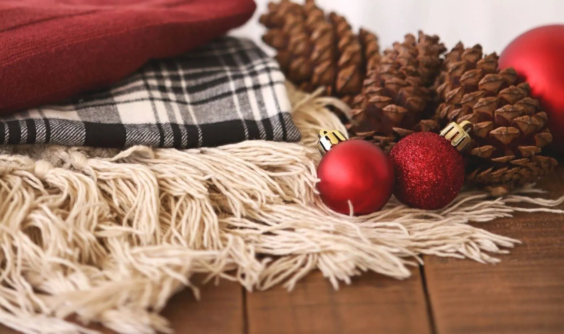 Cozy winter decor with plaid blanket, pinecones, and red ornaments.