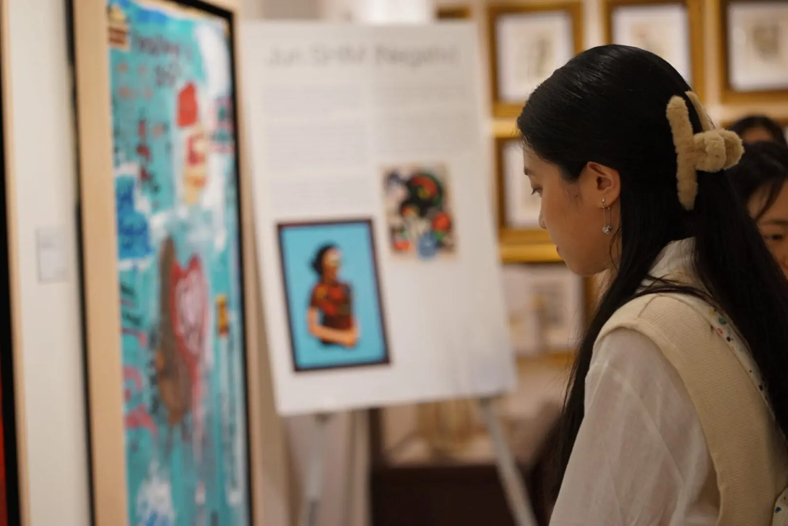A woman closely examines art pieces in a gallery.