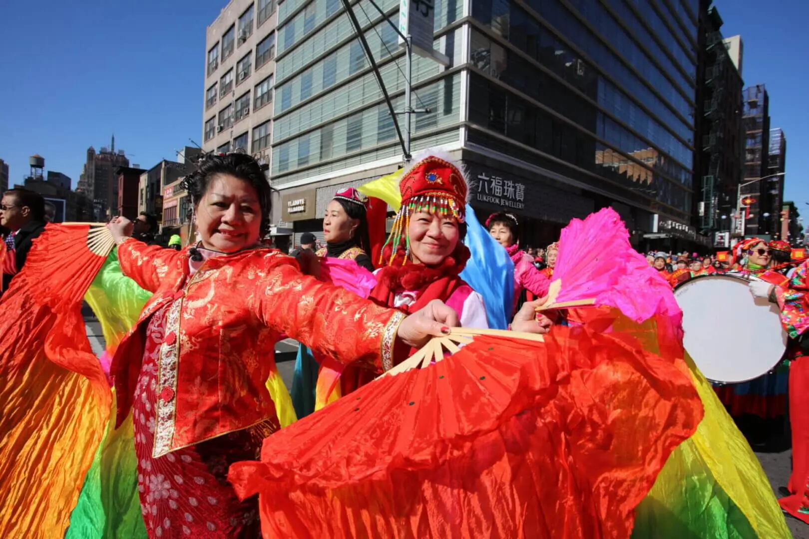 Two women in vibrant traditional dresses smiling outdoors in a city setting.