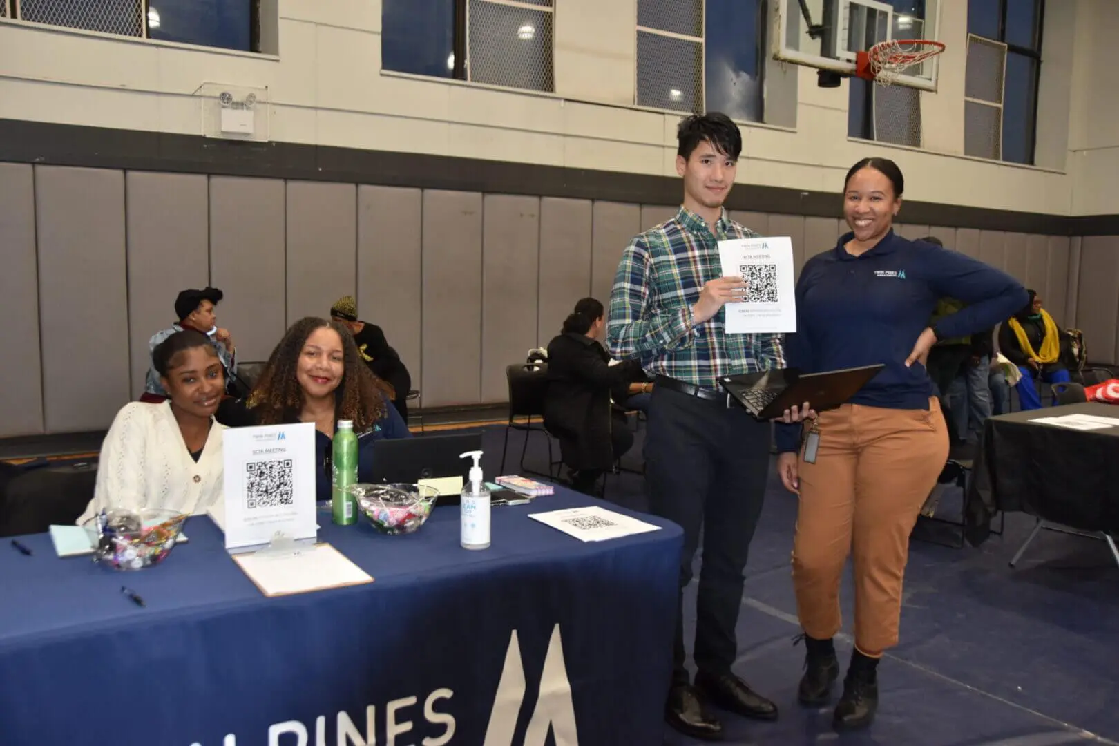 Two people at a table displaying QR codes in a gymnasium.