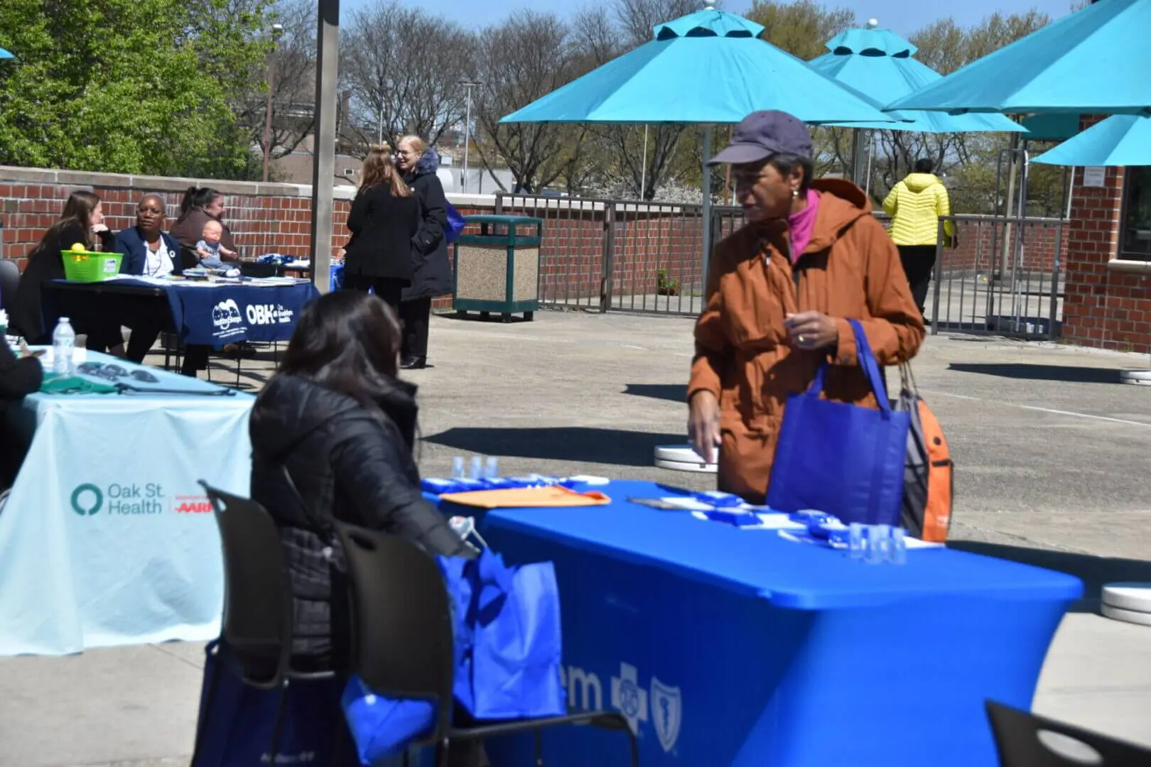 Two women interacting at an outdoor information booth with blue umbrellas.