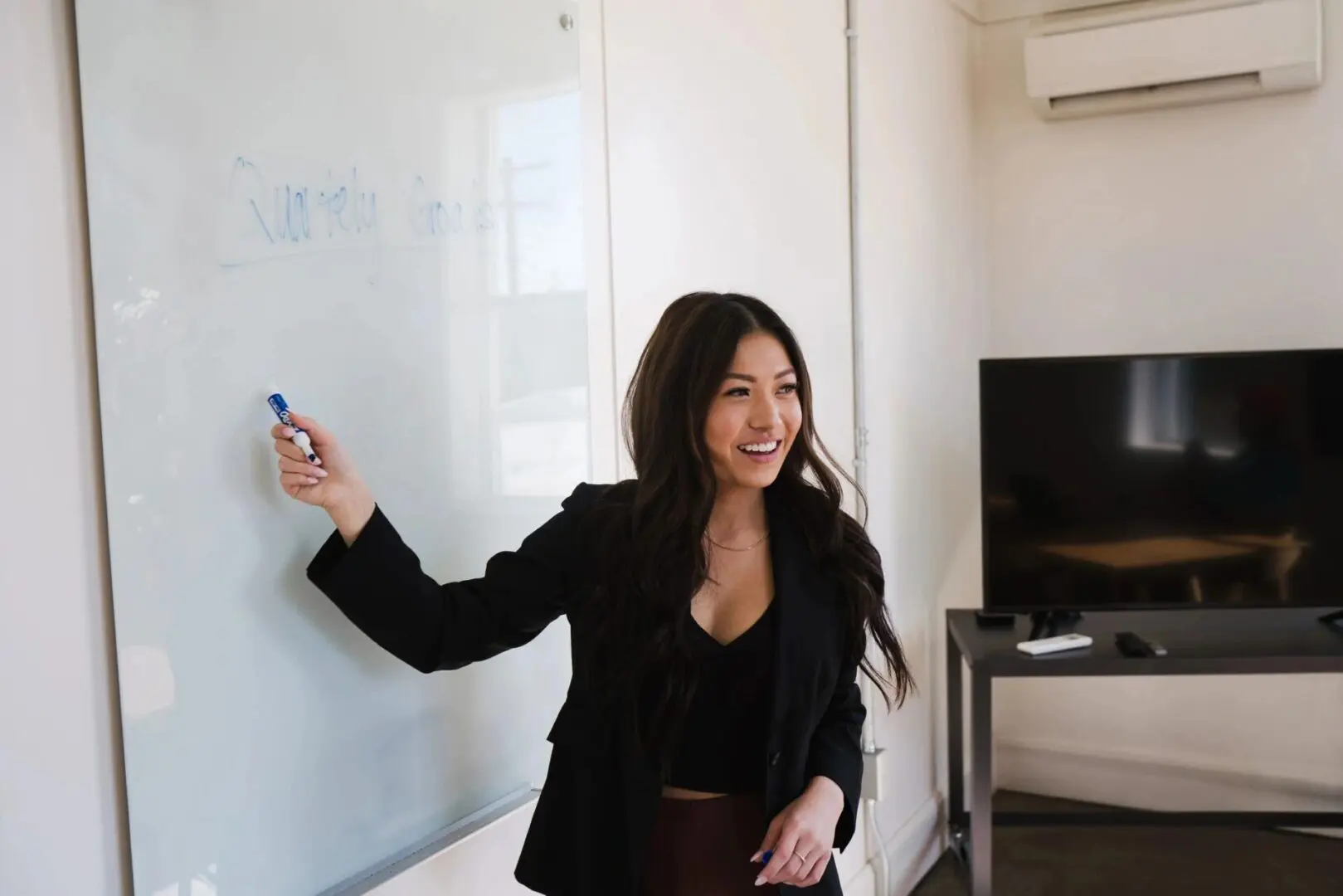 Woman smiling and pointing at a whiteboard in a meeting room.