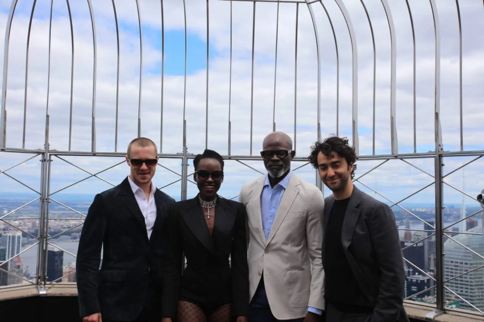 Four men in suits smiling outdoors with a cityscape background.