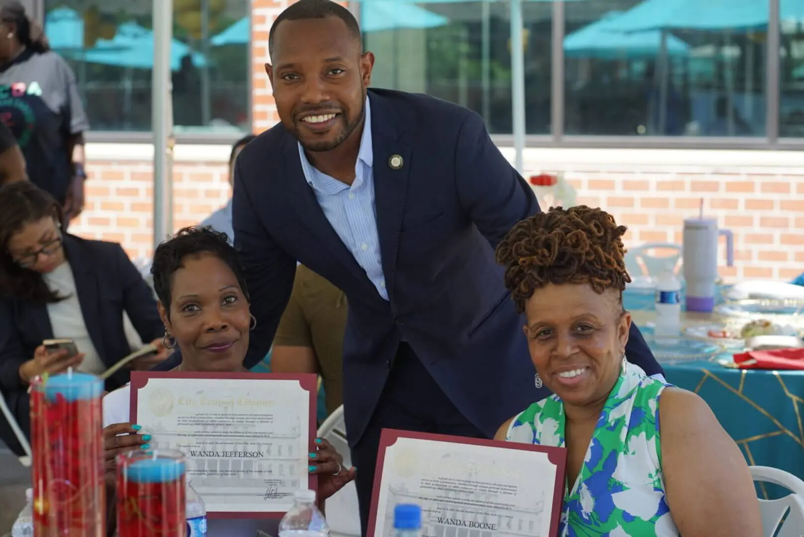 Three people smiling and holding certificates, with one man standing behind them.