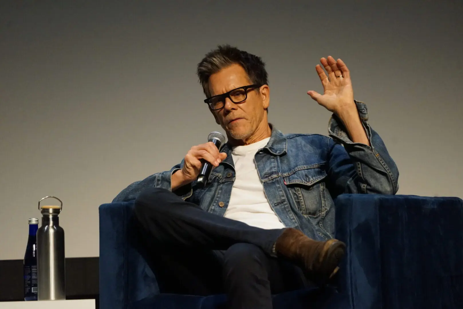 Man in denim jacket speaking into a microphone while seated.