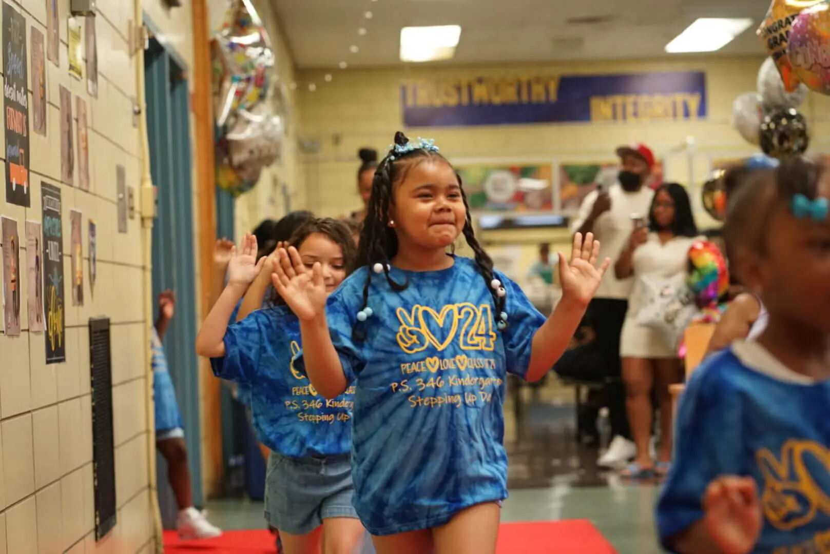 Young girls smiling and walking down a hallway during a school event.