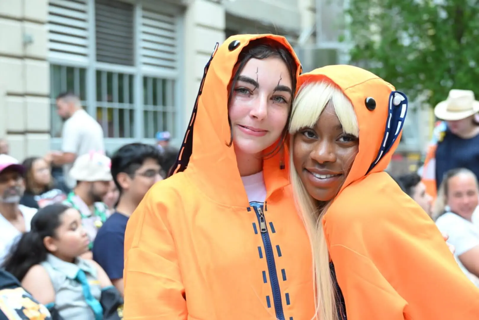 Two people smiling, wearing bright orange hooded costumes.