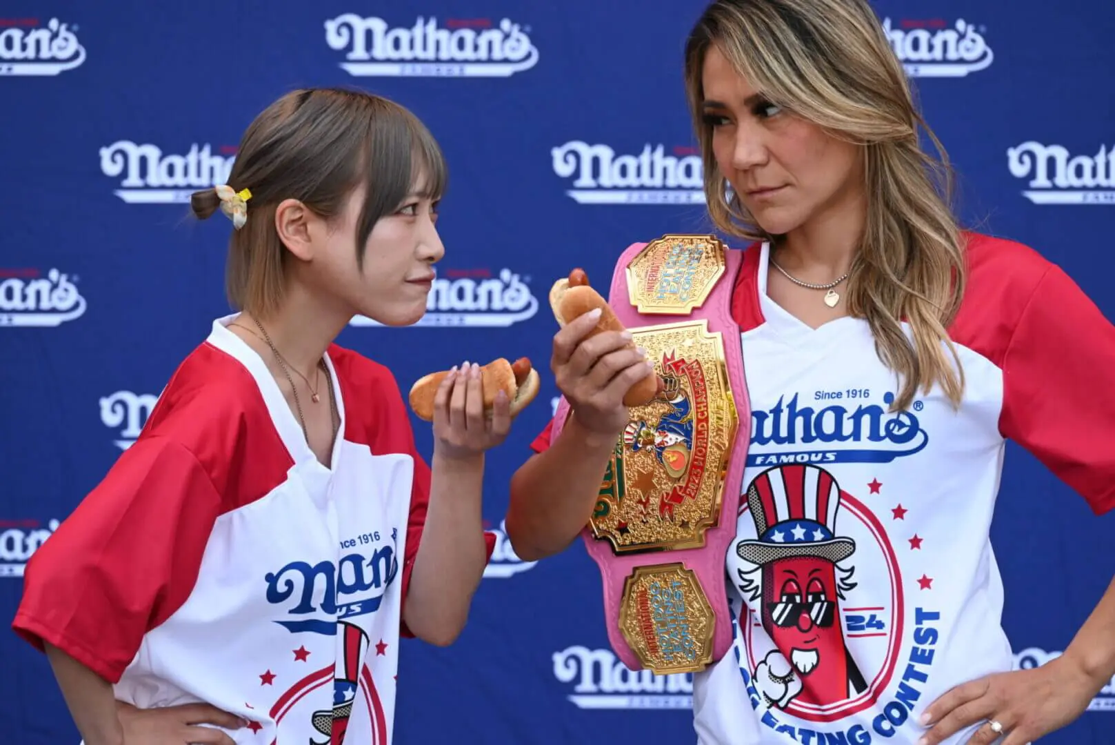 Two women holding hot dogs at a Nathan's Famous event.