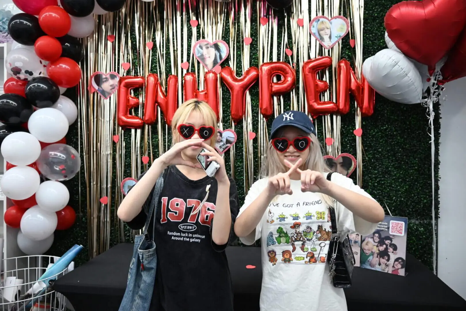 Two young people making heart shapes with their hands in front of a festive backdrop.