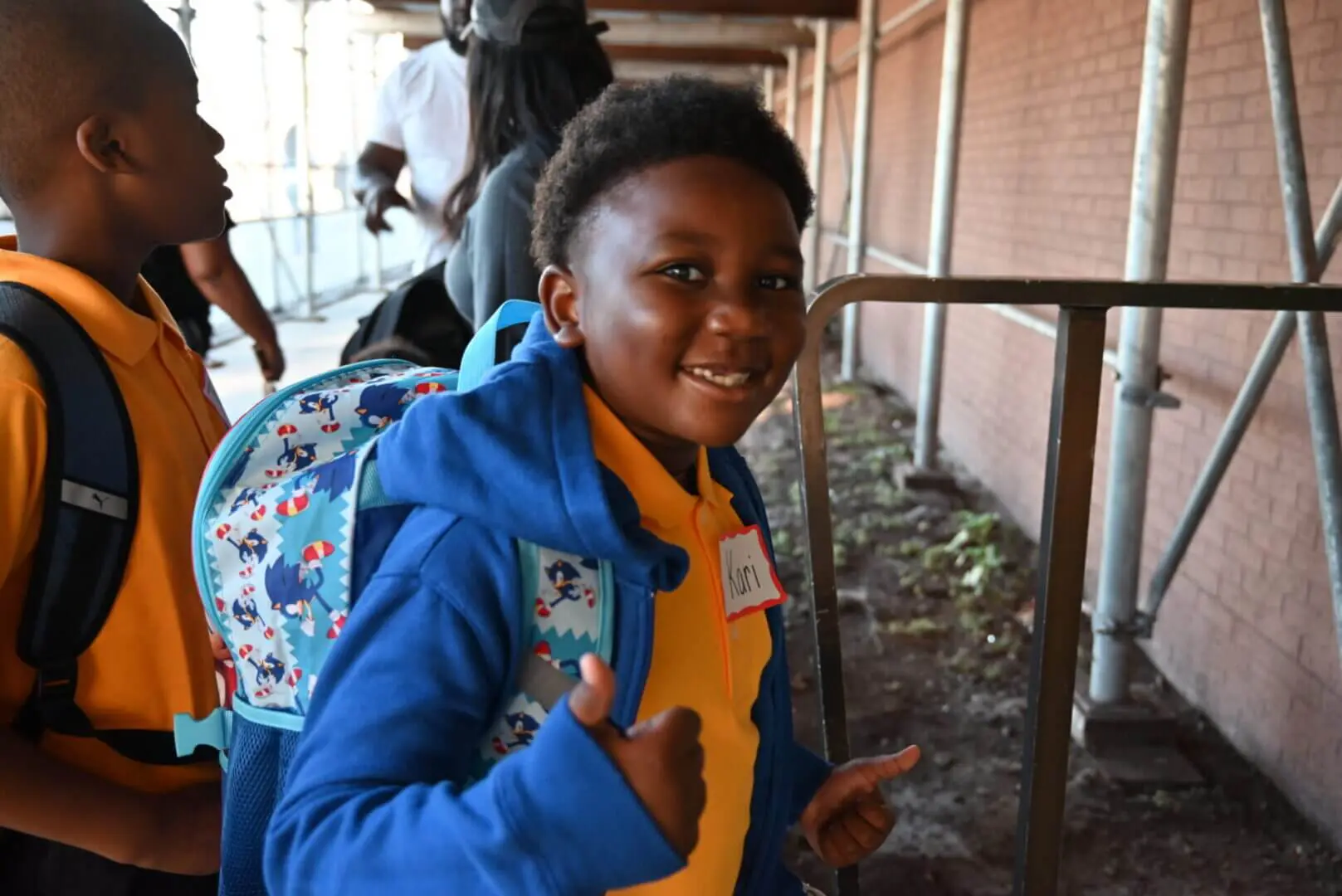 Smiling child in a blue jacket giving a thumbs-up gesture.