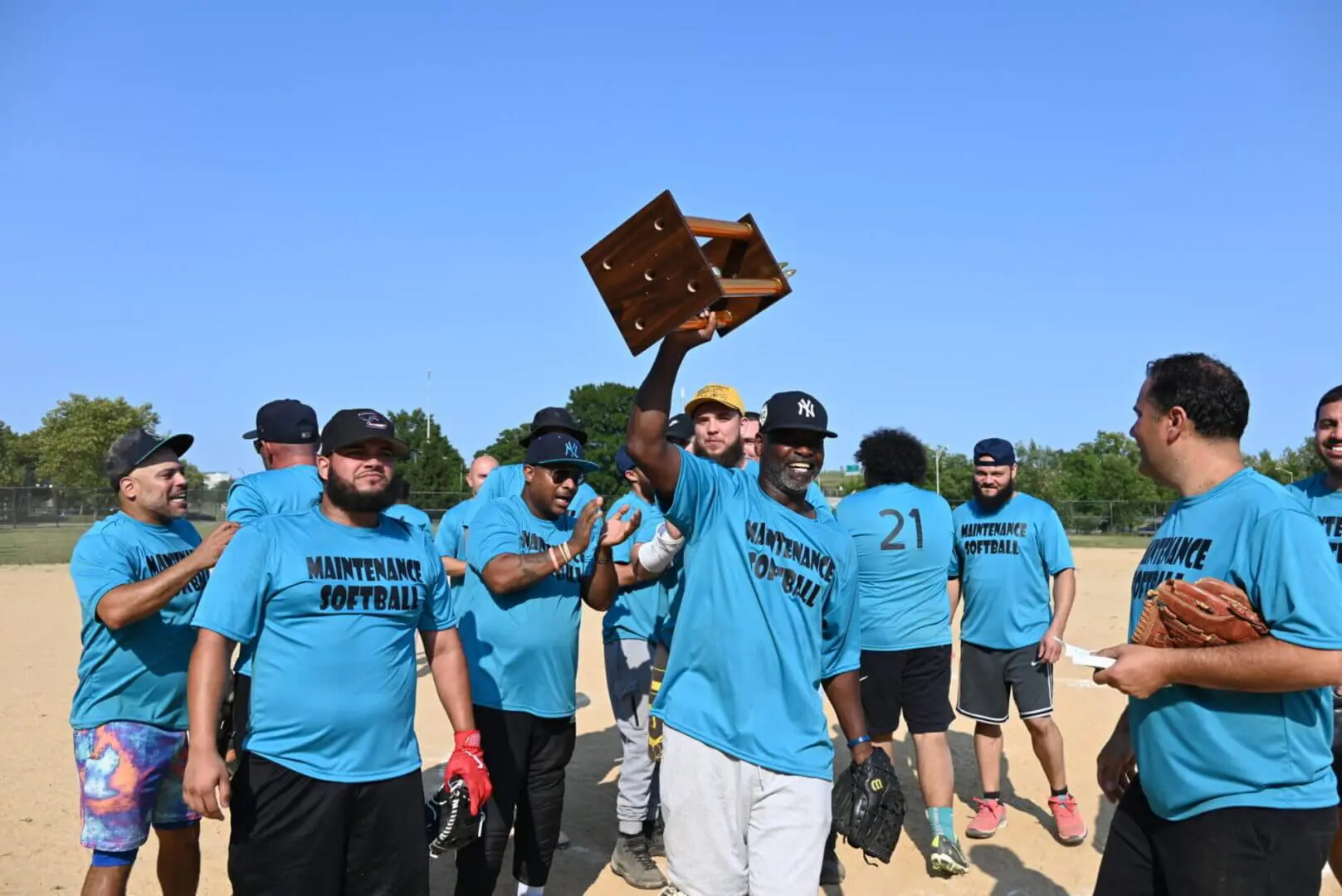 A group of men in teal shirts celebrating outdoors with a trophy.