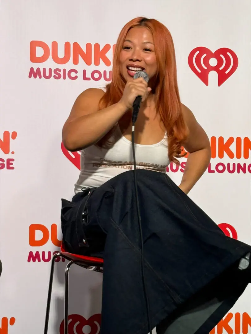Woman with long red hair speaks into a microphone at a Dunkin' event.