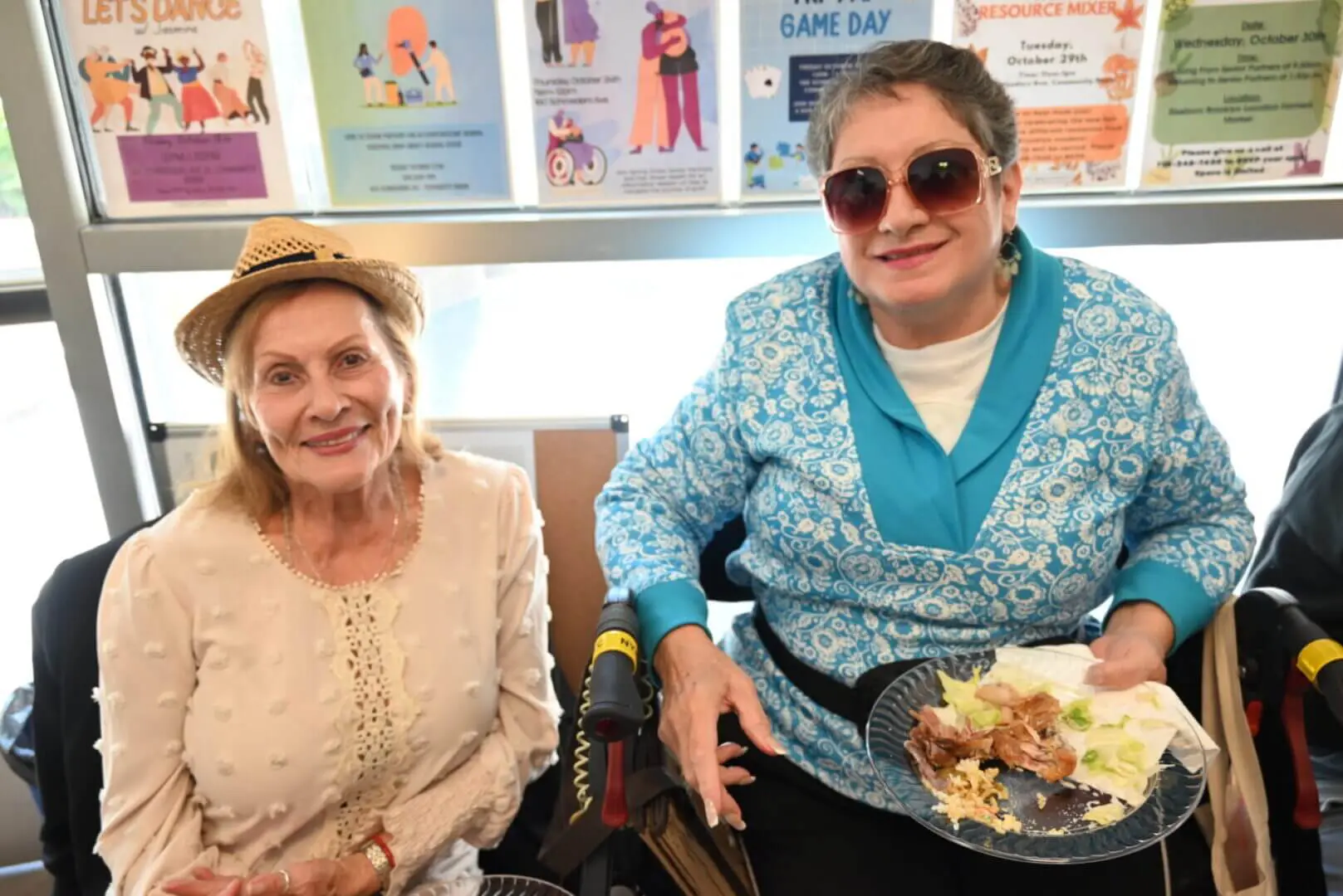 Two women smiling together, one holding a plate of food.