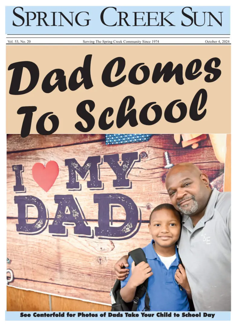 A father and daughter smiling with a 'Dad Comes To School' sign.
