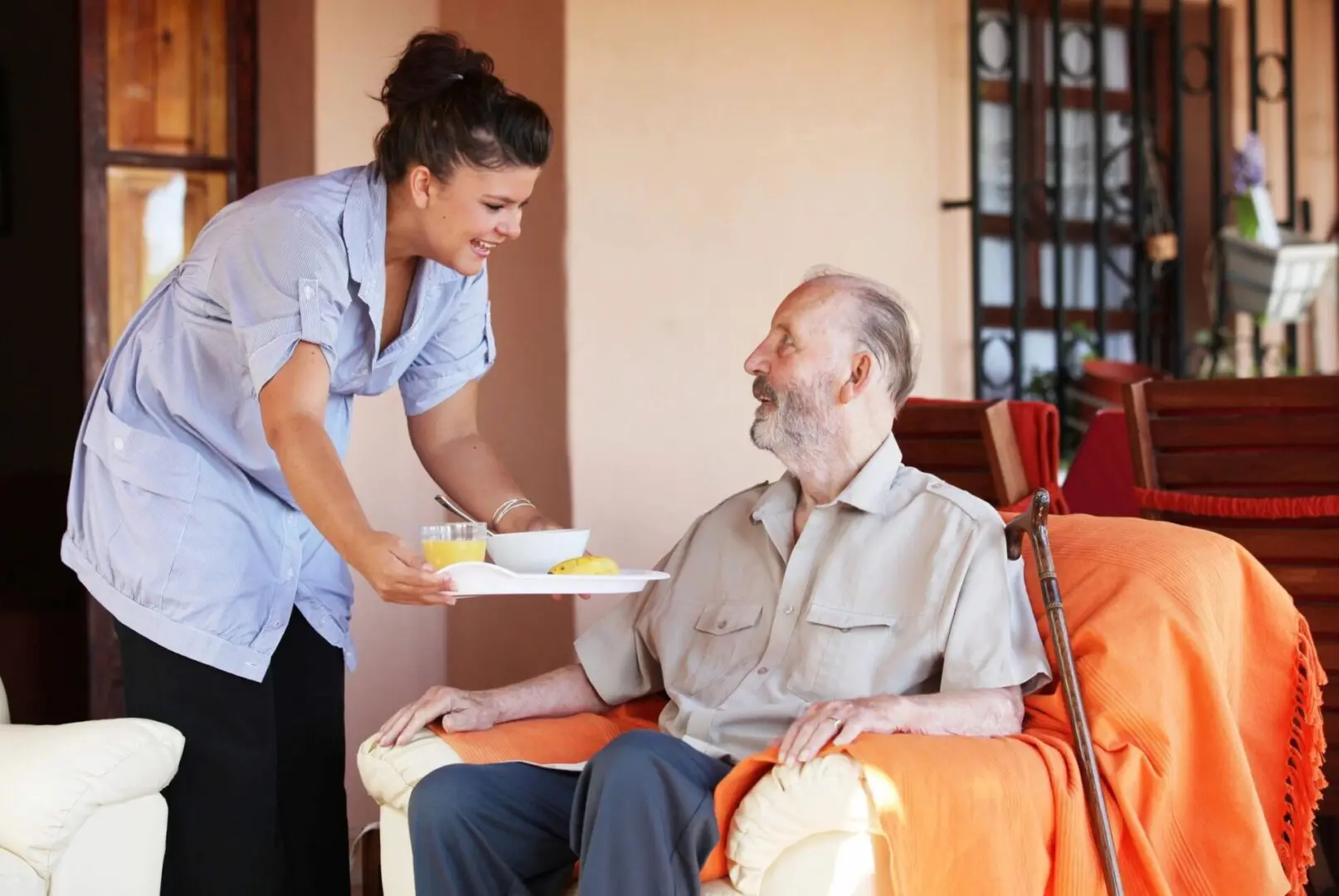 A caregiver serves a meal to an elderly man in a cozy room.
