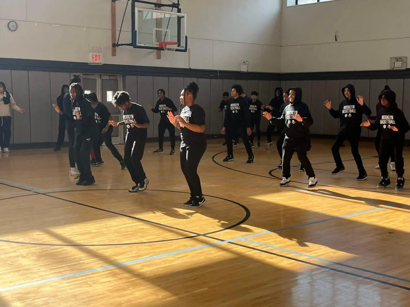 A group practicing martial arts in a gymnasium with sunlight streaming in.