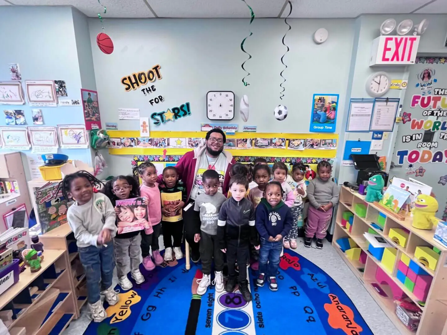 A group of young children and their teacher posing happily in a colorful classroom.