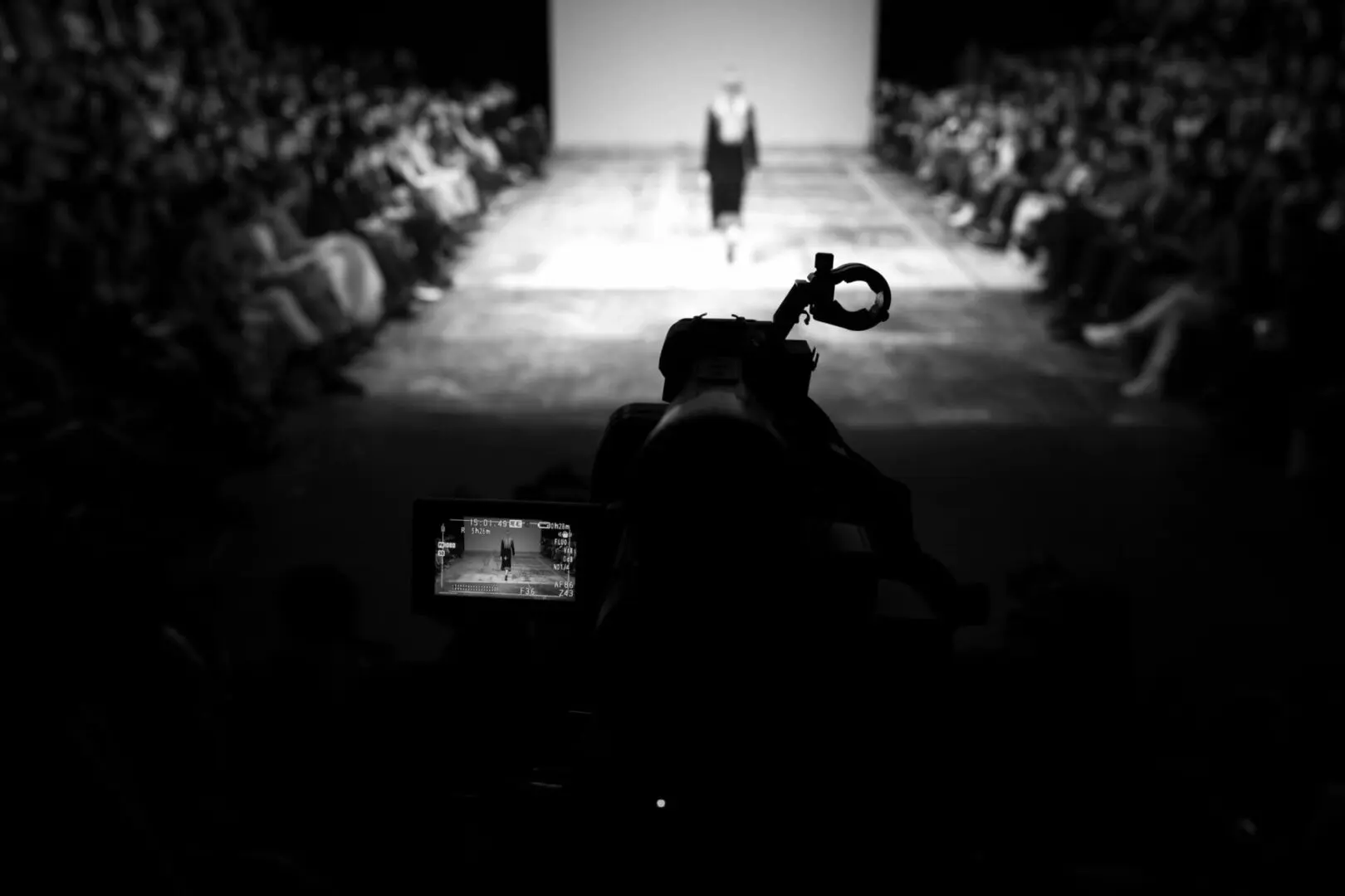 Black and white photo of a camera operator filming a runway show.