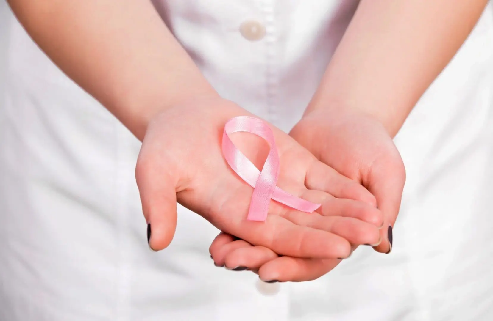 Hands holding a pink breast cancer ribbon.