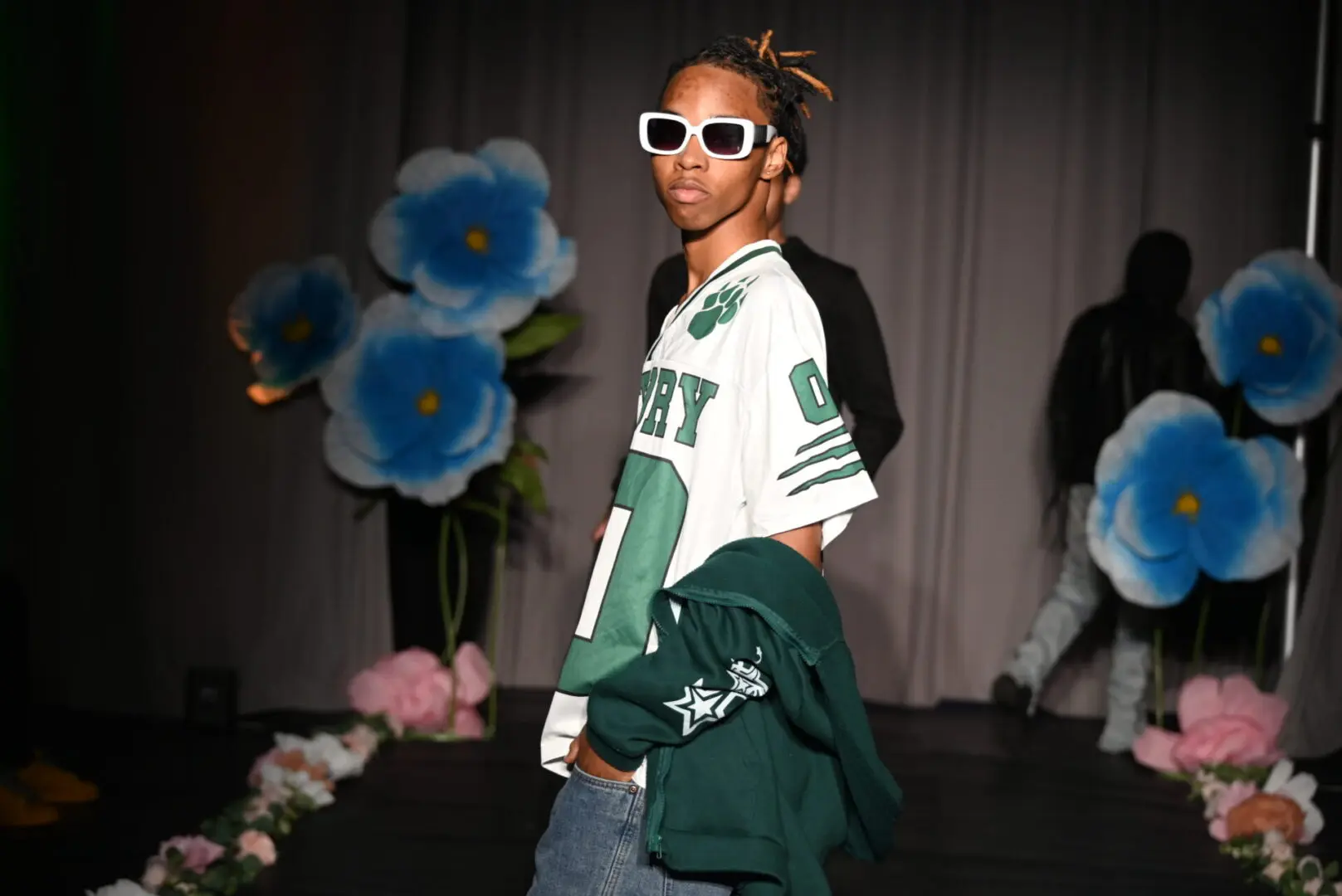 Model posing on fashion runway with flowers.