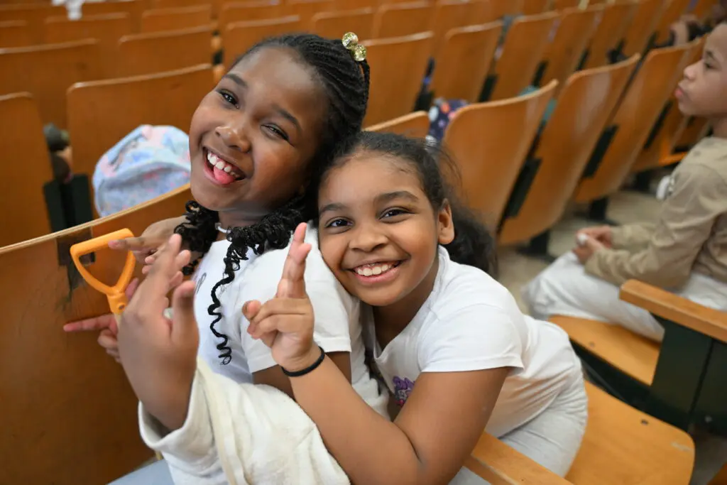 Two smiling girls sitting in auditorium seats.